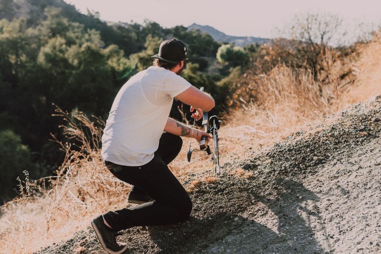 A man kneeling with a compound bow in a natural outdoor setting.